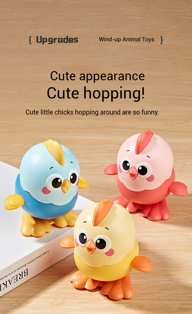 Three cute wind-up cartoon chick toys in blue, pink, and yellow are shown on a wooden surface.