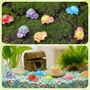 A collection of glow-in-the-dark turtle resin figurines in various colors scattered on green moss and colorful pebbles.