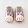 A pair of gray plush baby slippers shaped like rabbits with purple ears and anti-slip soles.