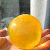 A hand holds a bright yellow, spherical coconut scented slow-rising squishy stress ball.
