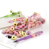 A collection of pink and purple silicone flower and leaf beads is displayed in a clear glass, next to a purple pen.