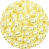 A close-up view of small, pale yellow imitation pearl beads scattered on a white background.