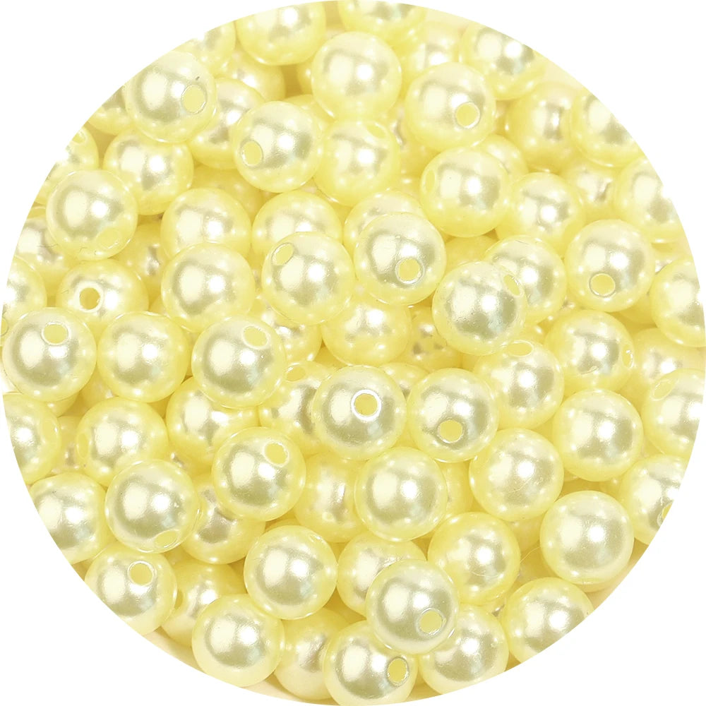 A close-up view of small, pale yellow imitation pearl beads scattered on a white background.