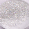 A pile of clear and iridescent glass rice beads in various sizes for DIY jewelry and crafting.