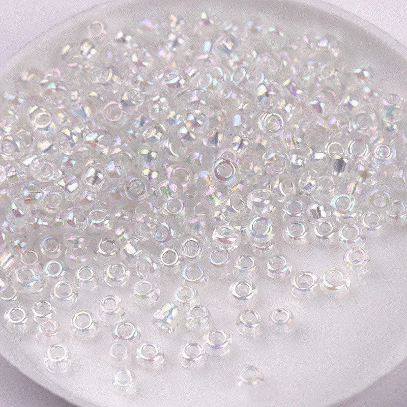 A pile of clear and iridescent glass rice beads in various sizes for DIY jewelry and crafting.
