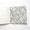 An open page of a black and white line drawing featuring detailed tropical leaves used for a mandala coloring book.
