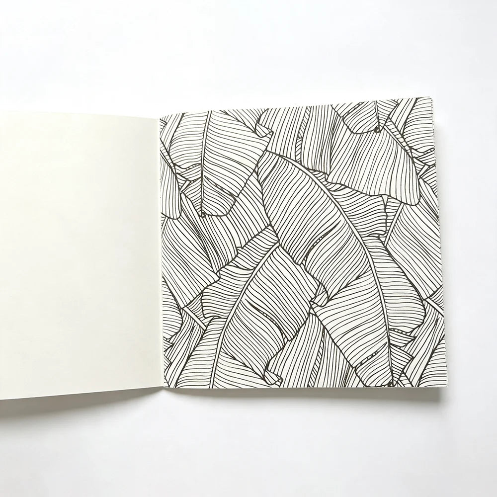 An open page of a black and white line drawing featuring detailed tropical leaves used for a mandala coloring book.