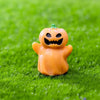 An orange cartoon pumpkin bear figurine sitting on bright green grass.