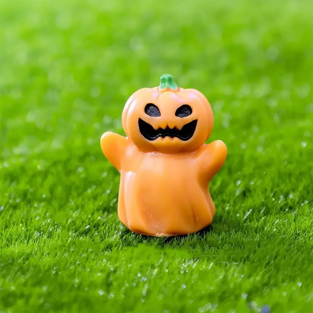 An orange cartoon pumpkin bear figurine sitting on bright green grass.
