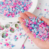A hand holds a pile of mixed resin rhinestone pearls in various shades of pink, blue, and purple for crafts and nail art.
