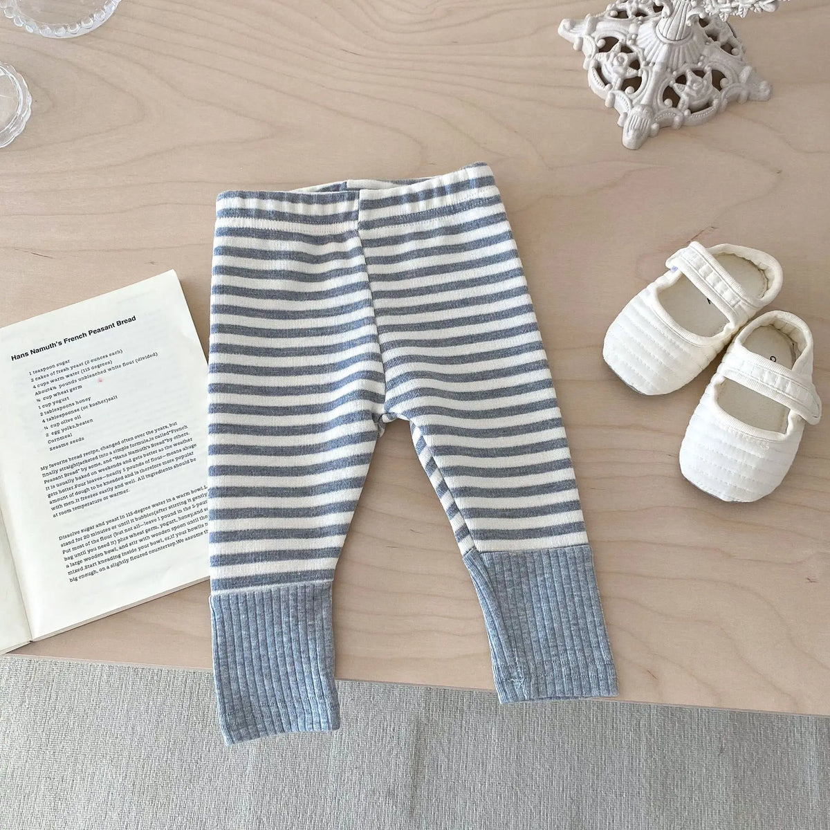 A pair of light blue and white striped baby leggings lying flat on a wooden surface next to a small white object.