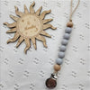 A wooden sun-shaped bead pacifier clip with a silicone teether and a string of gray beads.