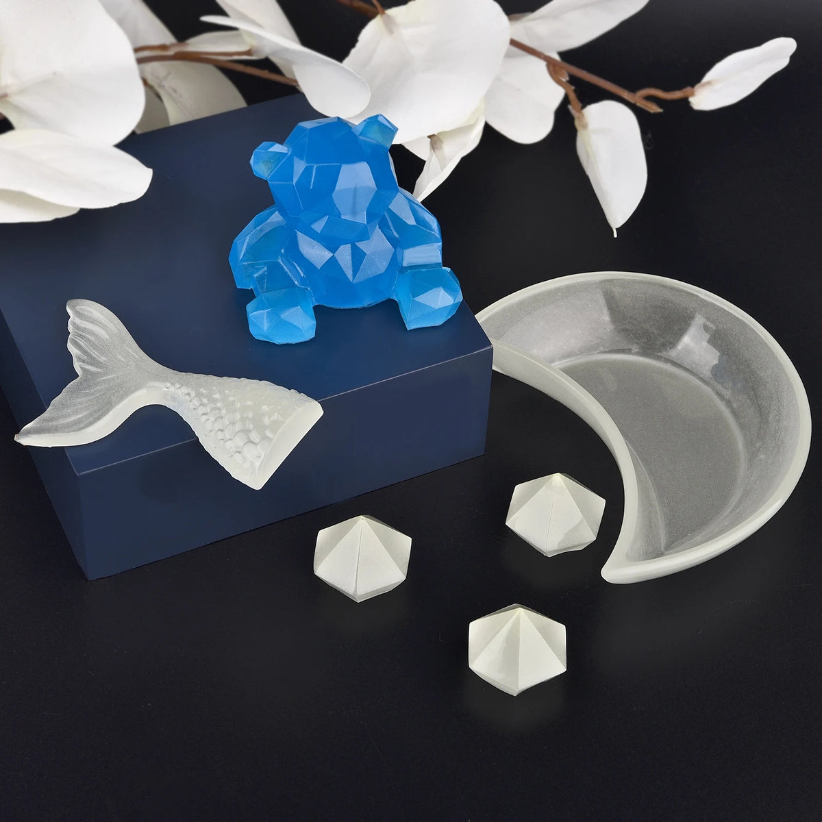 Blue glow-in-the-dark elephant figurine and white resin molds on a dark surface.