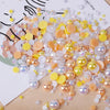 A close-up of mixed resin rhinestone pearls in shades of yellow, peach, and clear with an AB finish scattered on a white back
