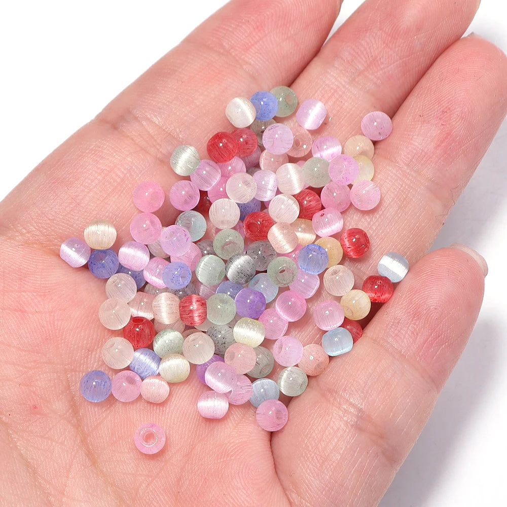 A handful of colorful 4mm cat eye glass beads in shades of pink, purple, and green for jewelry making