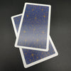 A vertical tarot card featuring a blue background with gold star patterns, lying next to another card.