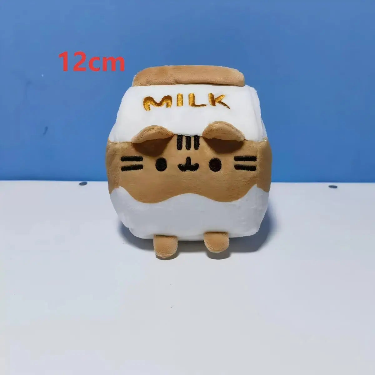 A white plush cat doll shaped like a milk carton with gold lettering, shown against a blue background.