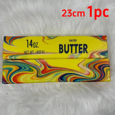 A rectangular yellow squishy butter toy with colorful marbled patterns is displayed on a white fluffy surface.