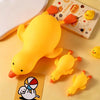 A bright yellow squishy toy shaped like a duck is shown on a light surface next to a book and a white plate.