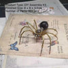 A finished steampunk metal spider DIY assembly kit with long legs and a dark body displayed on parchment paper.