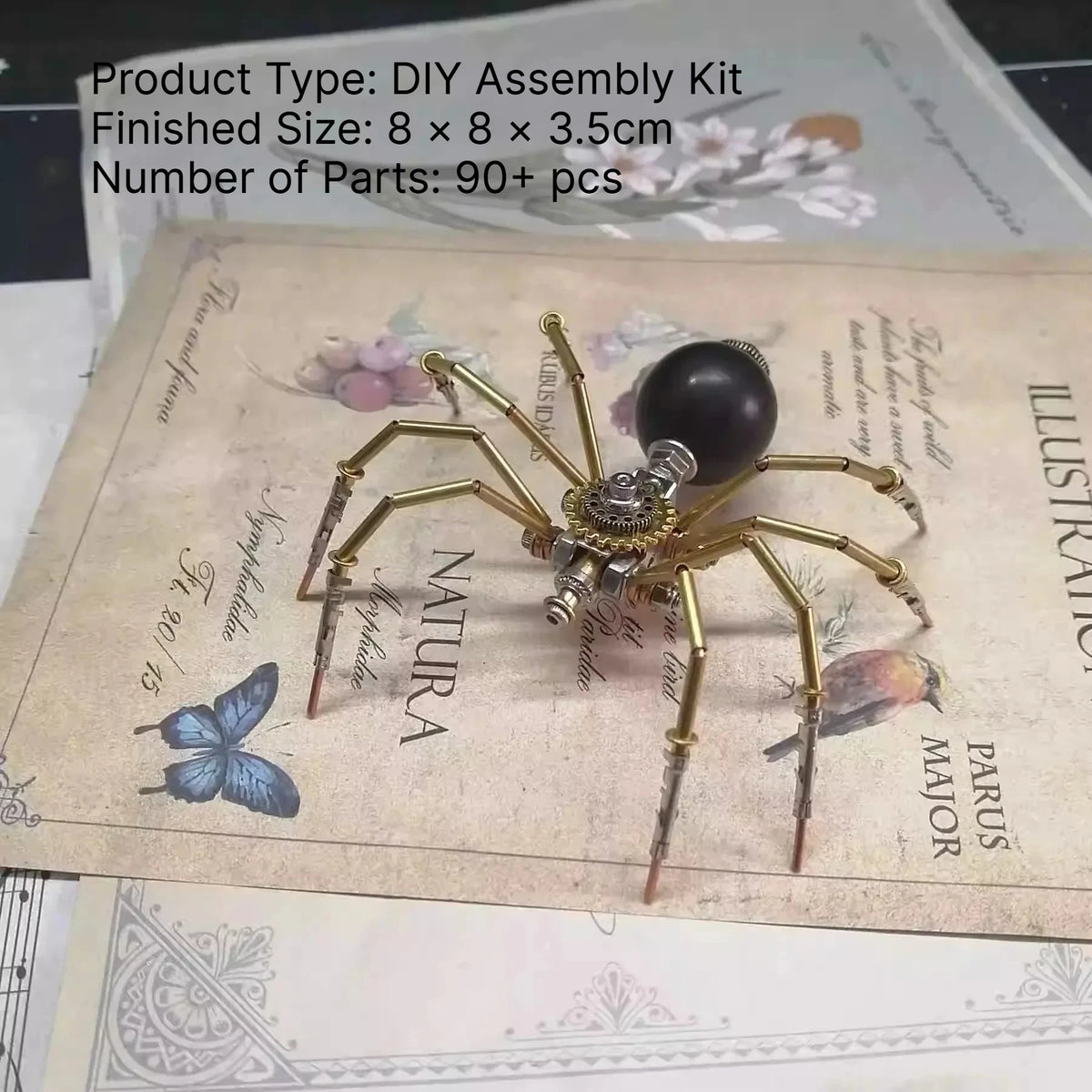 A finished steampunk metal spider DIY assembly kit with long legs and a dark body displayed on parchment paper.