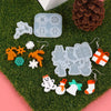 Silicone molds shaped like reindeer, snowflakes, and gifts for jewelry and craft projects on green moss.