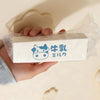 A white squishy toy labeled in Japanese text is held by a hand against a light background.