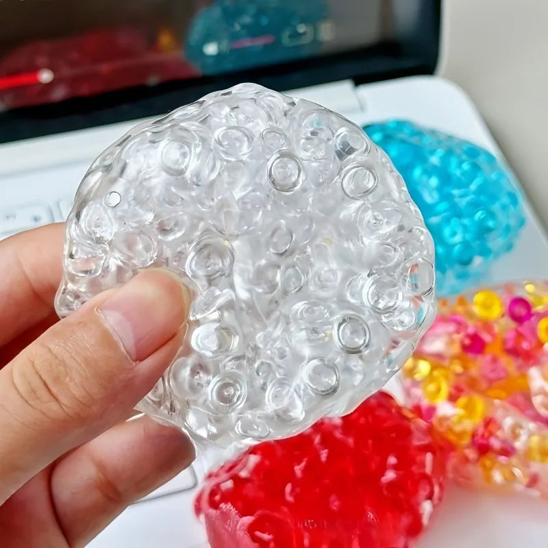 A hand holds a clear, spherical fidget ball toy with numerous small bubbles against a colorful background.