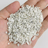 A hand holds a pile of white and gray natural tumbled stone chips for jewelry making and home decor.