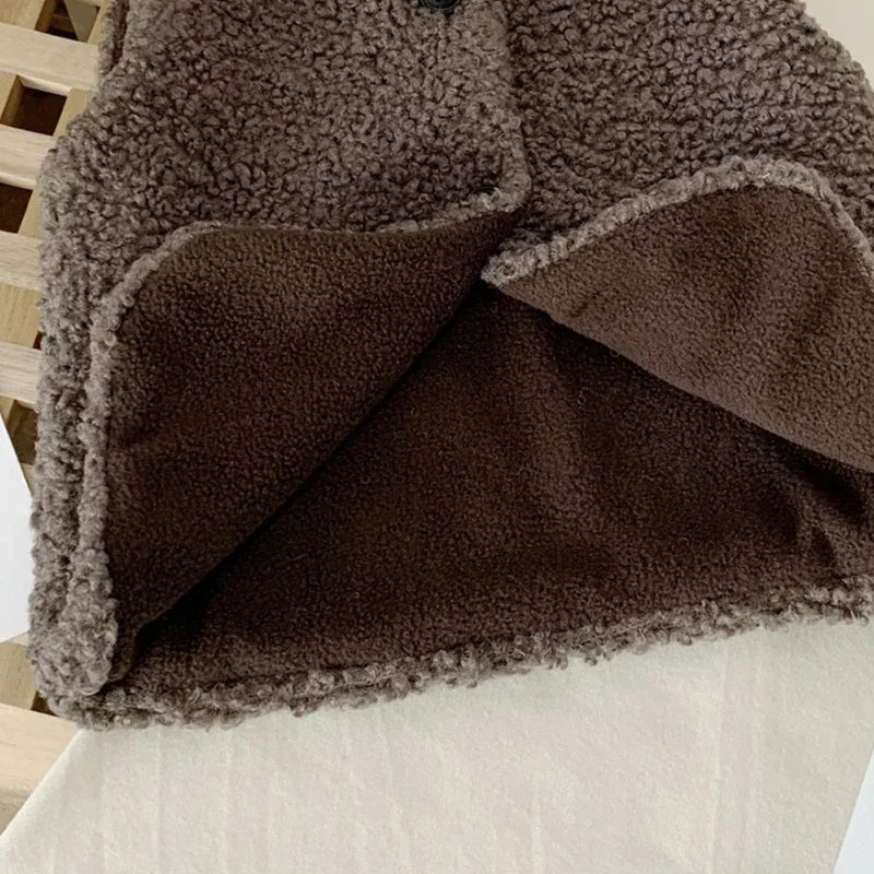 A close-up of a dark brown plush fleece vest with a contrasting tan panel, showing the texture and layered design.