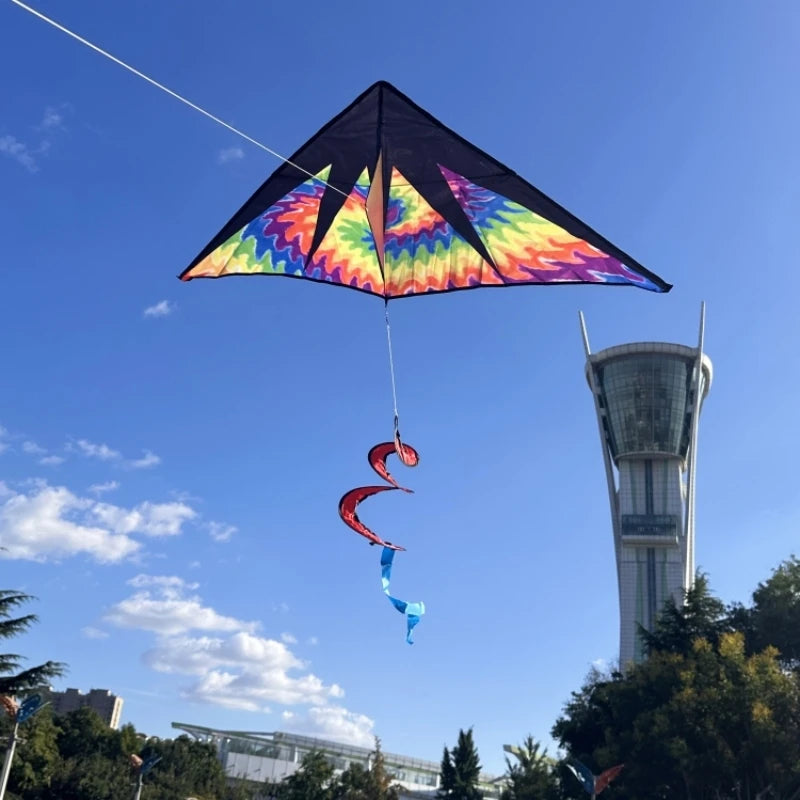 A colorful rainbow nylon kite is flying against a blue sky above a tall building.