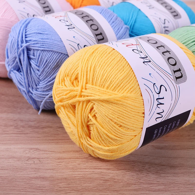 A close-up of several skeins of pure cotton knitting yarn in various colors, including blue and yellow, laid on a wooden surf