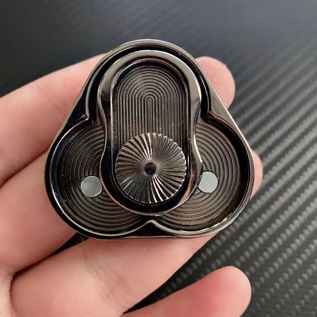 A close-up of a premium metal magnetic fidget slider with a ribbed design held in a hand.