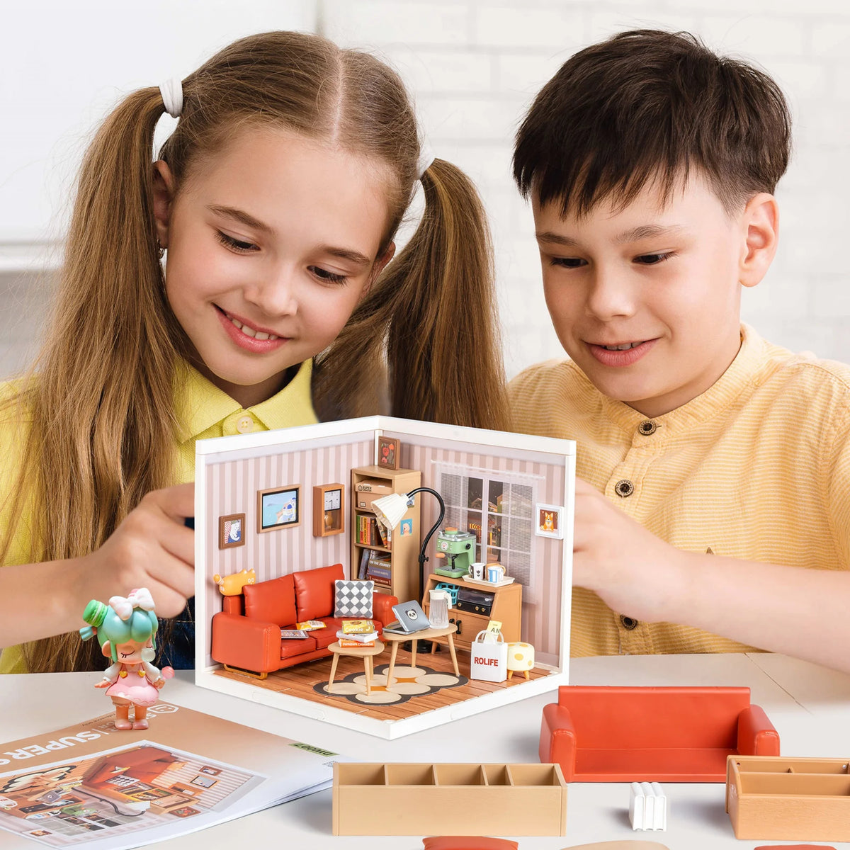 Two children look at a miniature house kit for DIY building with furniture and accessories.