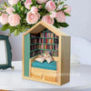 A wooden miniature bookshelf decor set filled with colorful books, displayed next to pink roses.