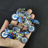 A motorcycle keychain fidget toy featuring blue and yellow paint with a silver frame and wheels, held in a hand.