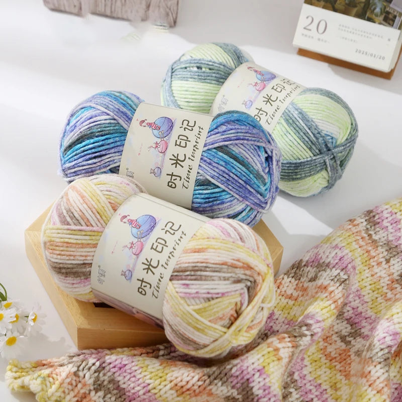 A stack of three balls of gradient acrylic yarn in shades of blue, green, and yellow resting on a wooden block.