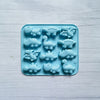 A silicone mold tray filled with small, light blue dinosaur shapes for baking and craft projects.