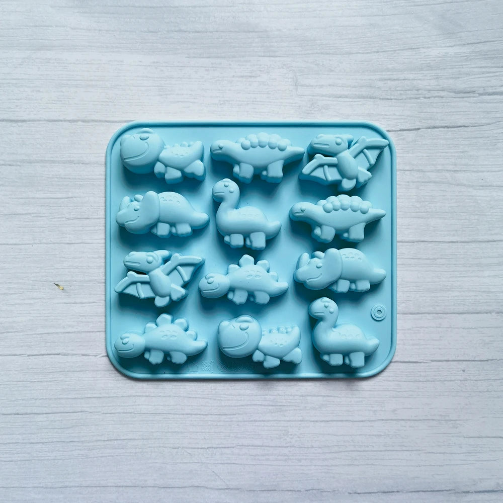 A silicone mold tray filled with small, light blue dinosaur shapes for baking and craft projects.