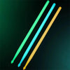 Three glow-in-the-dark nylon drumsticks in green, blue, and yellow are shown diagonally against a dark background.