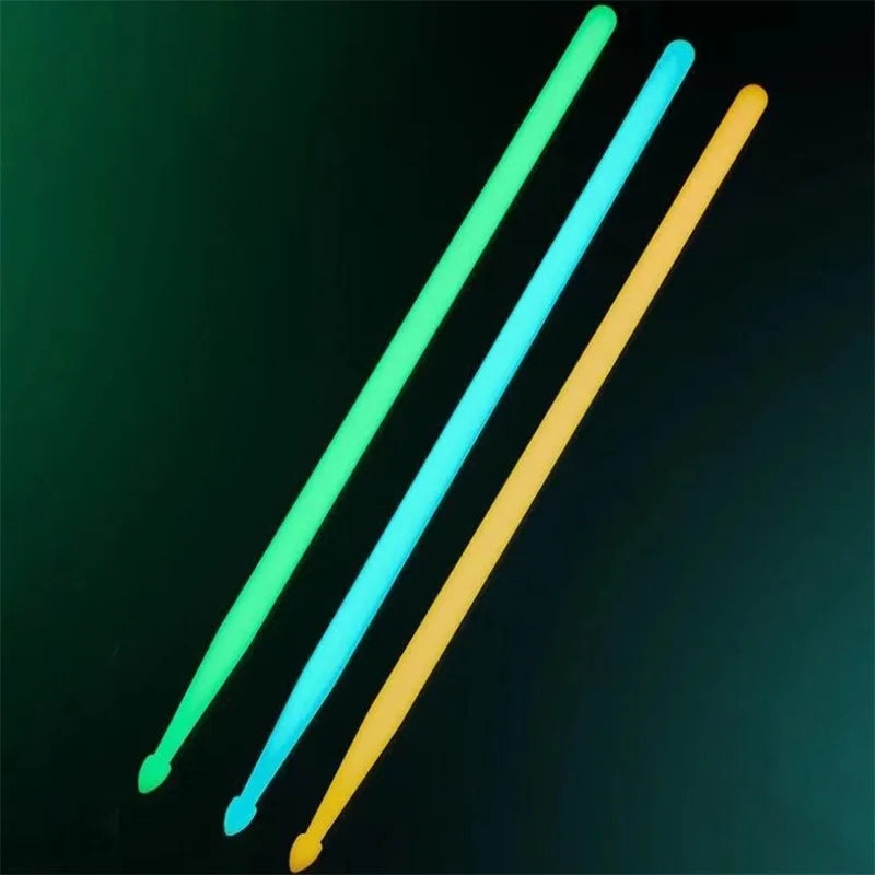 Three glow-in-the-dark nylon drumsticks in green, blue, and yellow are shown diagonally against a dark background.