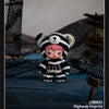 A small plush doll resembling a black and white striped bear is displayed outdoors on a blue surface.