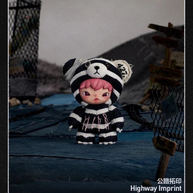 A small plush doll resembling a black and white striped bear is displayed outdoors on a blue surface.
