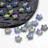 Small, colorful sakura flower crystal glass beads scattered on a dark stone surface.