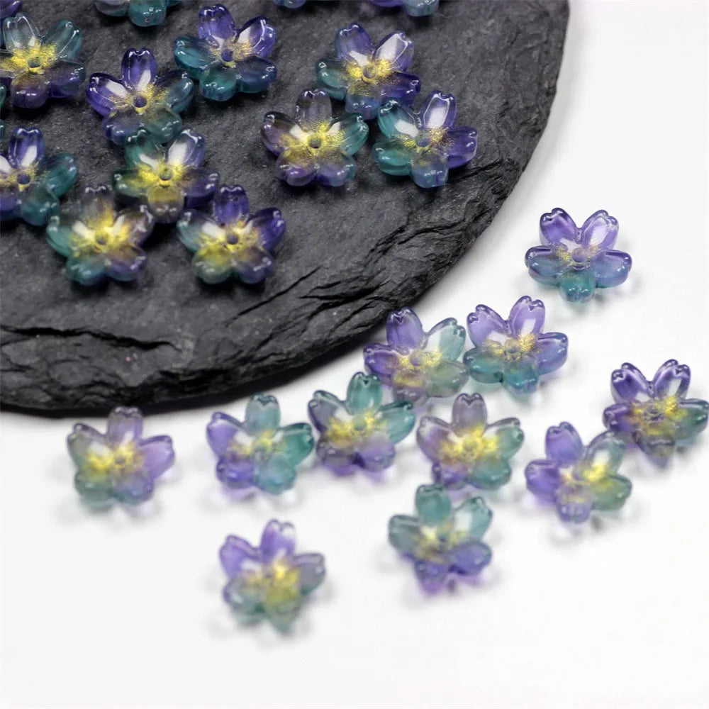 Small, colorful sakura flower crystal glass beads scattered on a dark stone surface.