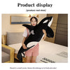 A woman is posing with a large black and white orca whale plush toy on a bed.