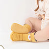 A pair of yellow cartoon animal non-slip socks for babies and toddlers lying on a white surface.