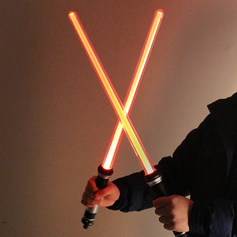 A person holds a glowing orange lightsaber toy with a bright yellow blade against a dark background.