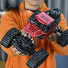 A person holds a red and black 4WD remote control stunt car off-road crawler truck with large tires.