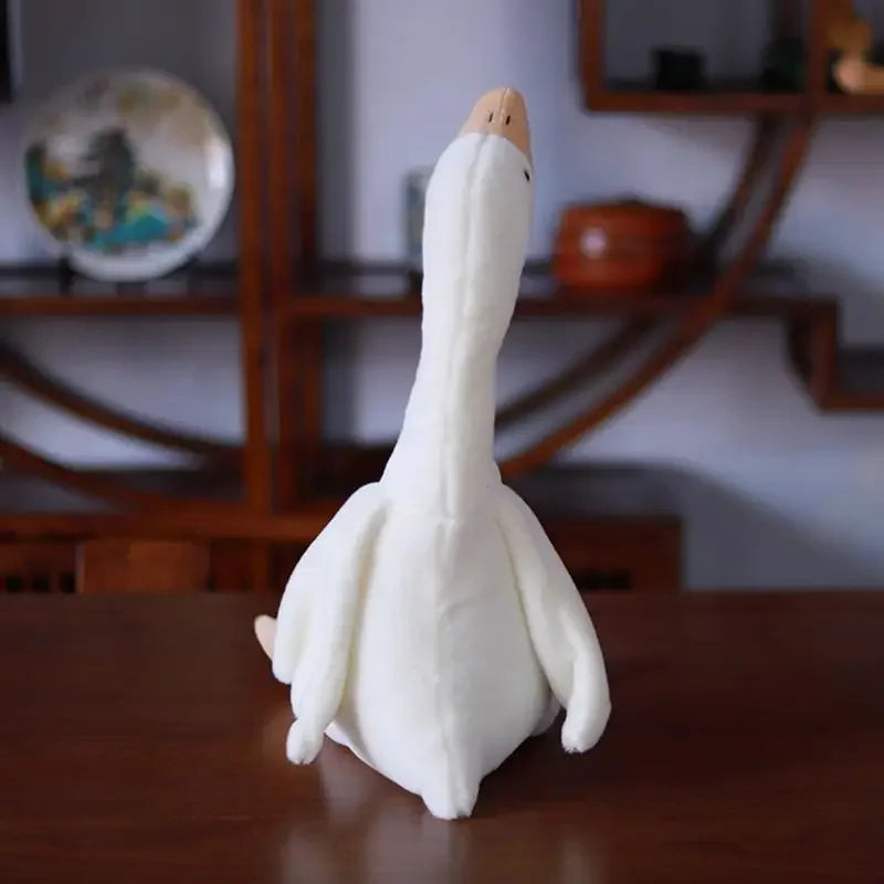 A white plush toy shaped like a goose with a long neck, resting on a wooden surface.